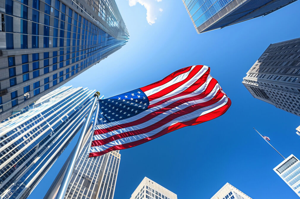 Bandeira dos Estados Unidos balançando no meio dos prédios na América, mostrando a importância de investir em internacionalização de empresas e entender como abrir empresa nos Estados Unidos.