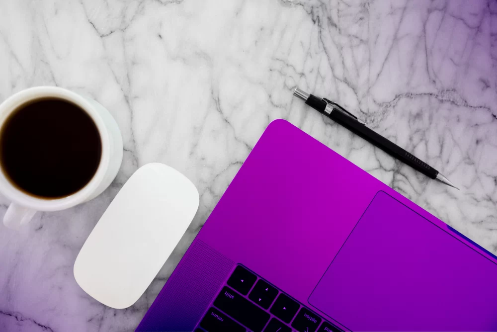 From above, a laptop sits atop a marble table, accompanied by a mousepad, a pen, and a cup of coffee. The setup hints the user is likely researching "Google Local Service Ads for Construction" while enjoying coffee.