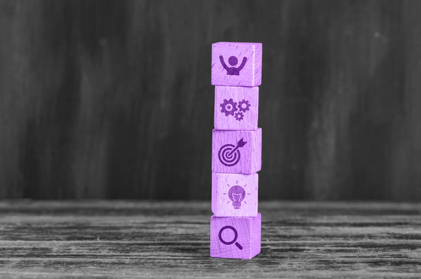 Blocos de madeira da cor roxa, com vários ícones representando a inteligência de mercado, empilhados um em cima do outro.